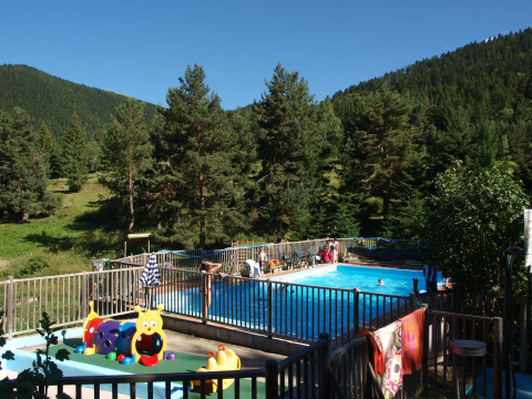 Piscina exterior en Base Lodge, Camping Les Sapins, rodeada de montañas y bosque en Francia.