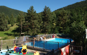 Udendørs swimmingpool ved Base Lodge, Camping Les Sapins, omgivet af skovklædte bjerge i Frankrig.