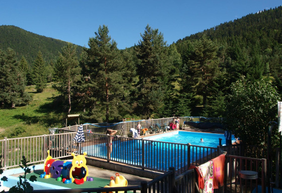 Piscine extérieure du Base Lodge, Camping Les Sapins en France, entourée de montagnes boisées.