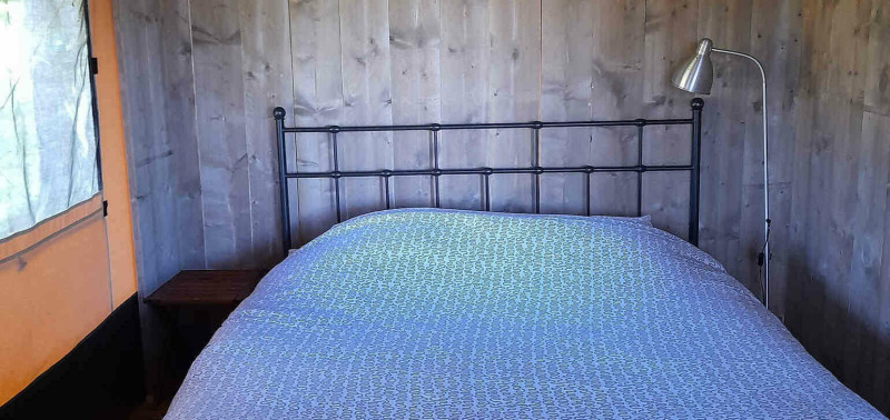 Schlafzimmer im Safarizelt Base Lodge auf Camping Les Sapins in Frankreich mit Doppelbett und Lampe.