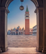 Vista a través de un arco hacia la Plaza de San Marcos en Venecia con la basílica y el campanario al amanecer.