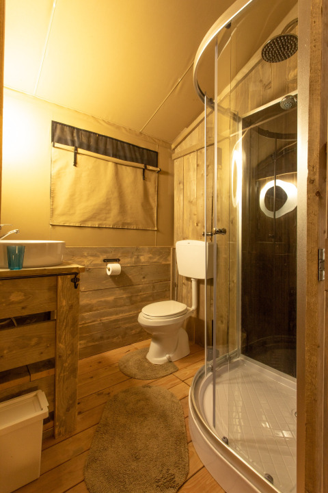Baño de la tienda safari Wood Lodge en Camping Al Lago di Lago, Italia, con interior de madera rústica.