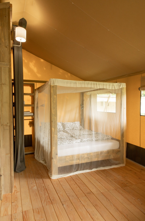 Vista interior de una tienda safari Wood Lodge con cama con dosel y mosquitera en Camping Al Lago di Lago, Italia.