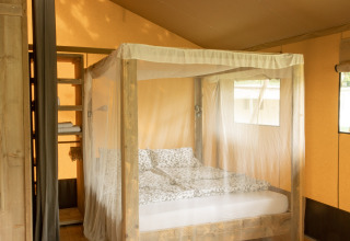 Vista interior de una tienda safari Wood Lodge con cama con dosel y mosquitera en Camping Al Lago di Lago, Italia.