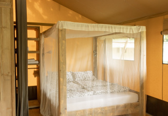Vista interior de una tienda safari Wood Lodge con cama con dosel y mosquitera en Camping Al Lago di Lago, Italia.