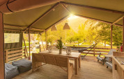 Terraza cubierta de la tienda safari Wood Lodge con mesa de madera en Camping Al Lago di Lago, Italia.