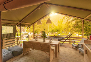 Terraza cubierta de la tienda safari Wood Lodge con mesa de madera en Camping Al Lago di Lago, Italia.