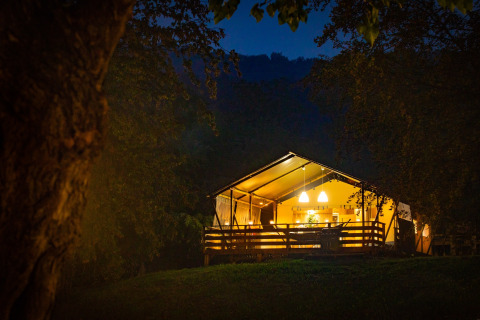 Tienda safari iluminada en Wood Lodge, Camping Al Lago di Lago, Italia, resplandeciendo en el bosque nocturno.