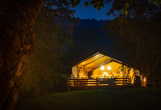 Tienda safari iluminada en Wood Lodge, Camping Al Lago di Lago, Italia, resplandeciendo en el bosque nocturno.