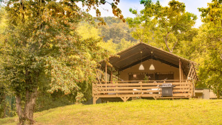 La tienda tipo safari Wood Lodge en una colina verde, rodeada de árboles, bajo un cielo soleado.