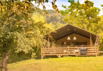 La tienda tipo safari Wood Lodge en una colina verde, rodeada de árboles, bajo un cielo soleado.