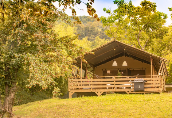 La tienda tipo safari Wood Lodge en una colina verde, rodeada de árboles, bajo un cielo soleado.