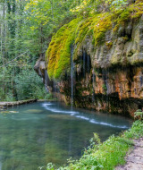 Escena tranquila en el bosque cerca de Berdorf, Luxemburgo, con un acantilado musgoso y un estanque claro.