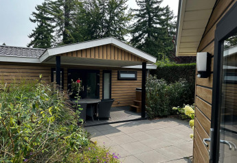 Udendørs terrasse og indgang til Family Lodge med spabad på De Thijmse Berg, omgivet af grønne planter.