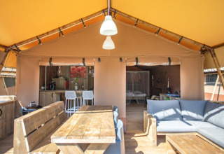 Vista interior de la tienda safari Desert Lodge XL en Camping Gajole, Italia, con muebles de madera y sofá.