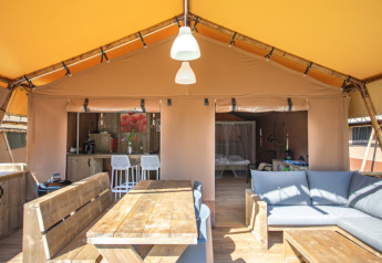 Vista interior de la tienda safari Desert Lodge XL en Camping Gajole, Italia, con muebles de madera y sofá.