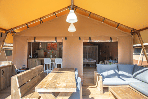 Innenansicht des Desert Lodge XL Safari-Zelts auf Camping Gajole in Italien mit Holzmöbeln und Sofa.