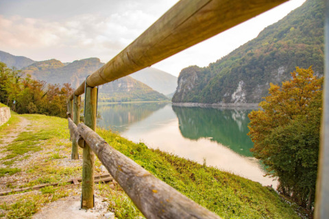 Vista su lago e montagne al Camping Gajole in Veneto, Italia, con sentiero naturale e staccionata in legno.