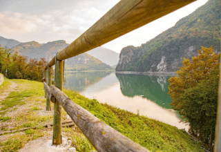 Lake and mountain view at Camping Gajole in Veneto, Italy, with nature trail and rustic wooden railing.
