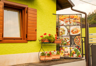 Buitenscène bij Camping Gajole in Veneto met groene gevel, houten raam en menubord van gerechten.