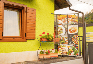 Outdoor view at Camping Gajole in Veneto, Italy with green wall, wooden window and food menu sign.