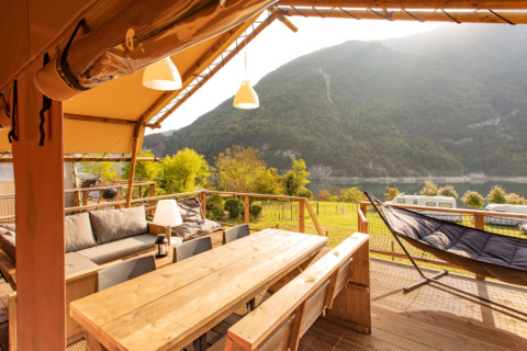 Veranda in legno del Desert Lodge XL a Camping Gajole, Italia, con vista su lago e montagne circostanti.
