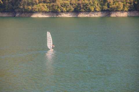 Windsurfista navegando en el lago de Camping Gajole, Véneto, Italia, con colinas verdes al fondo.