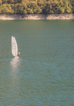 Windsurfista navegando en el lago de Camping Gajole, Véneto, Italia, con colinas verdes al fondo.