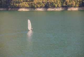 Windsurfer op het meer bij Camping Gajole in Veneto, Italië, met beboste heuvels op de achtergrond.