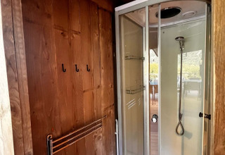 Cabina de ducha moderna y pared de madera con ganchos en una tienda safari de Big Oak Lodge, vista exterior.