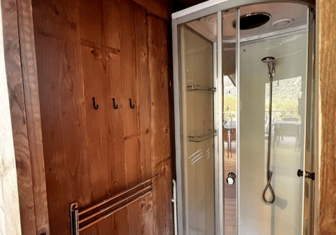 Cabina de ducha moderna y pared de madera con ganchos en una tienda safari de Big Oak Lodge, vista exterior.