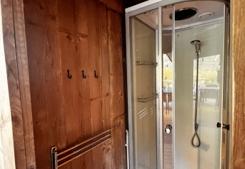 Modern shower cabin and wooden paneled wall with hooks inside a safari tent at Big Oak Lodge, view outside.