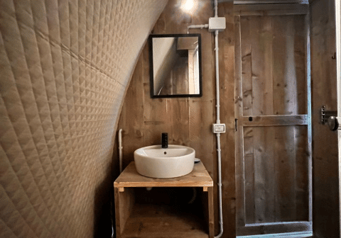 Innenaufnahme des Safari-Zeltes Big Oak Lodge mit Holzwänden, rundem Waschbecken und Spiegel.