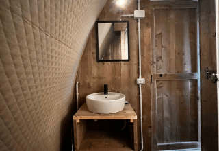 Foto interior de la tienda Safari Big Oak Lodge con paredes de madera, lavabo redondo y espejo.