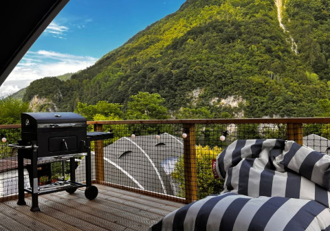 Terraza exterior del Big Oak Lodge en Camping Gajole, Italia, con parrilla, puff y vistas a la montaña.