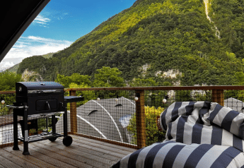 Terraza exterior del Big Oak Lodge en Camping Gajole, Italia, con parrilla, puff y vistas a la montaña.