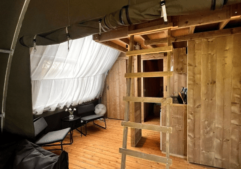 Interno della tenda safari Big Oak Lodge con pavimento in legno, scala, salottino e grandi tende bianche.