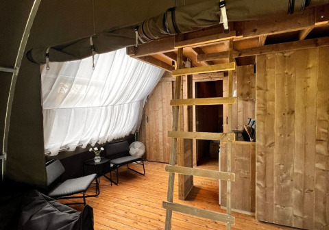 Binnenkant van de Big Oak Lodge safaritent met houten vloer, ladder, zithoek en grote gordijnen.