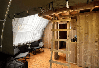 Interno della tenda safari Big Oak Lodge con pavimento in legno, scala, salottino e grandi tende bianche.