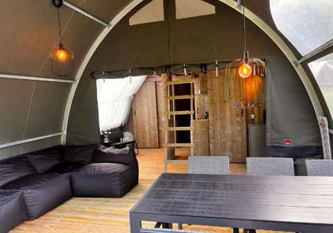 Interieur van de Big Oak Lodge safaritent met zwarte zetel, eettafel, houten wand en sfeervolle verlichting.