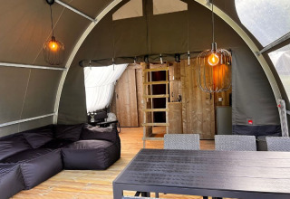 Interior de la tienda safari Big Oak Lodge con sofá negro, mesa de comedor, pared de madera y lámparas colgantes.