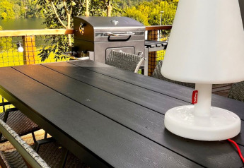 Außenbereich eines Safari-Zeltes Big Oak Lodge mit Grill, Sitzgruppe und weißer Lampe auf dem Tisch.