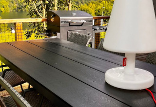 Área de comedor exterior en la tienda safari Big Oak Lodge con parrilla, sillas y una lámpara blanca grande.