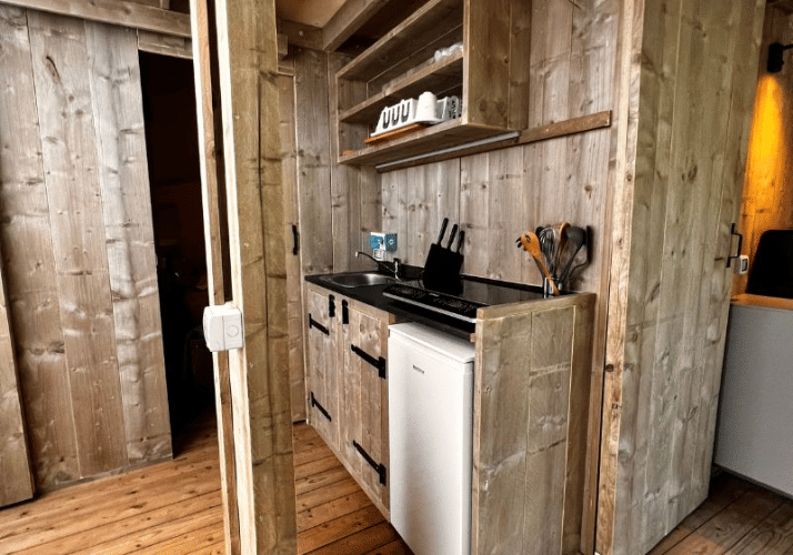 Compact kitchenette inside the Big Oak Lodge safari tent with a mini fridge, sink, and cooking utensils.