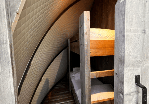 Vista interna della tenda safari Big Oak Lodge con letti a castello e pareti curve imbottite in legno.