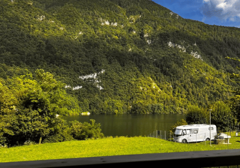 Vista dalla tenda safari Big Oak Lodge su una montagna boscosa, lago e camper sotto il sole.