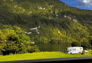 Vista desde la tienda safari Big Oak Lodge a una montaña boscosa, lago y autocaravana al sol.