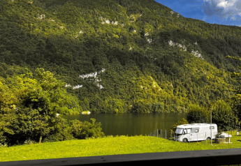 Vista desde la tienda safari Big Oak Lodge a una montaña boscosa, lago y autocaravana al sol.