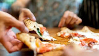 Primer plano de varias manos compartiendo porciones de pizza en una mesa de madera en un parque vacacional con glamping.