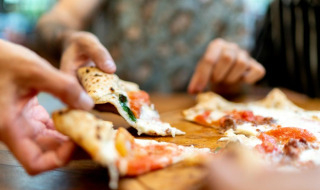 Primer plano de varias manos compartiendo porciones de pizza en una mesa de madera en un parque vacacional con glamping.